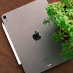 Top view of a sleek tablet and stylus on a brown surface beside a green plant.